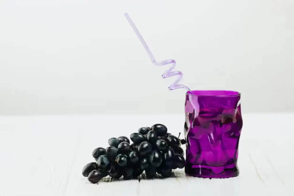 Glass of water and grapes on plain background